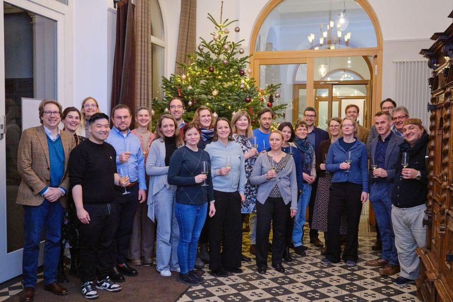 Eine Gruppe von Personen steht drinnen vor einem Weihnachtsbaum.